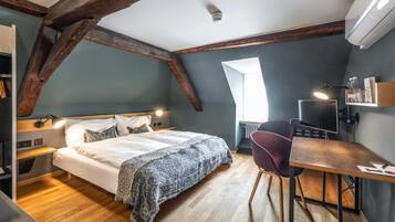 A bedroom with a large bed, a desk, and a chair. There is a window providing natural light.