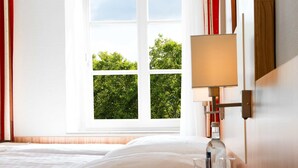Una habitación de hotel con una cama, una mesita de noche con lámpara y una ventana con cortinas.