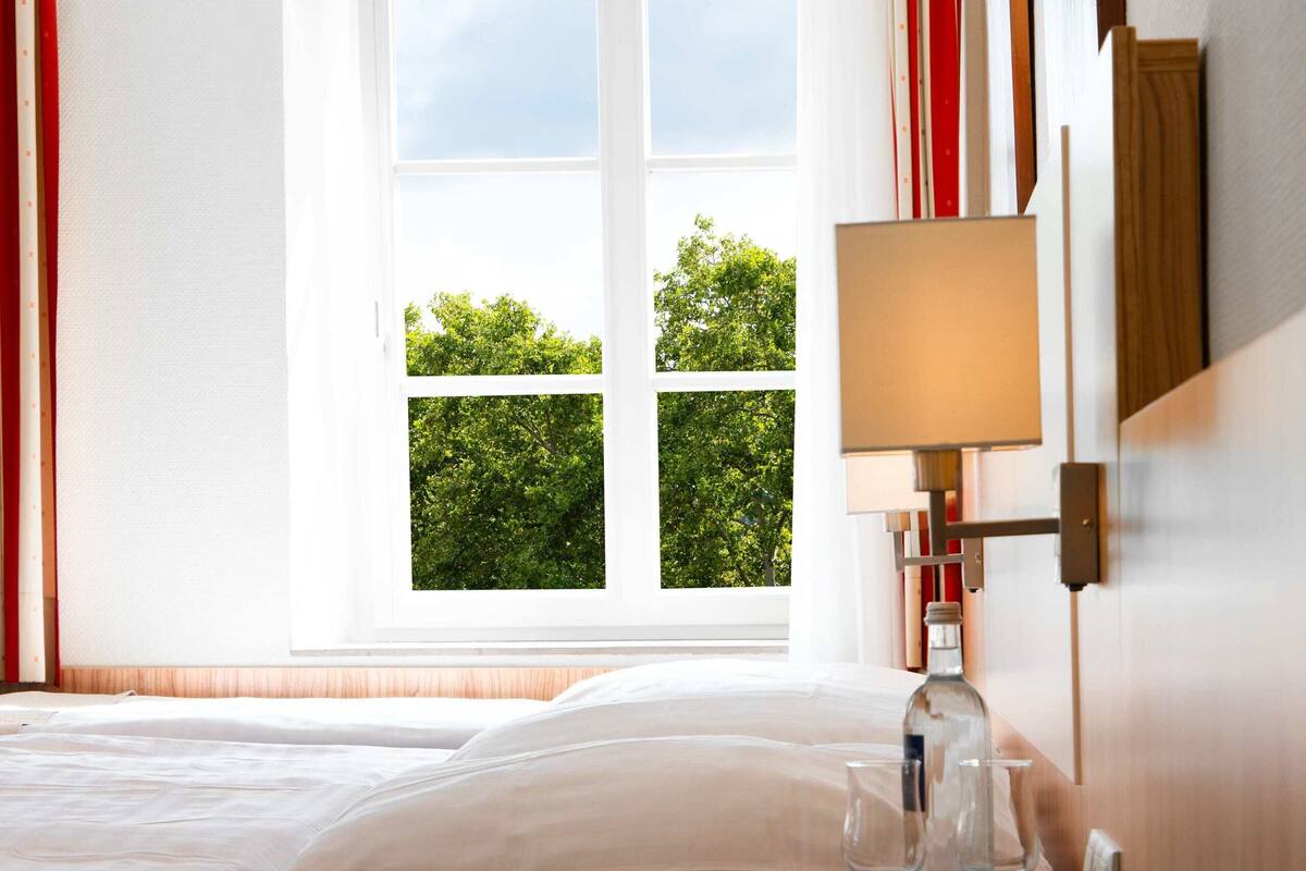 Una habitación de hotel con una cama, una mesita de noche con lámpara y una ventana con cortinas.