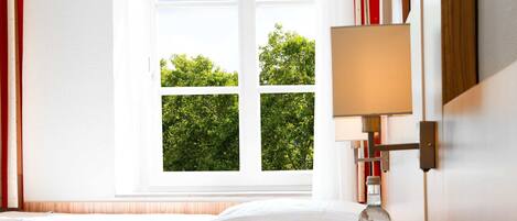Una habitación de hotel con una cama, una mesita de noche con lámpara y una ventana con cortinas.