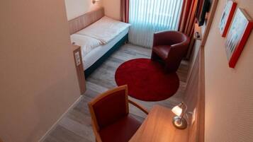 Una habitación de hotel con una cama, una silla roja, un escritorio de madera y una alfombra roja.