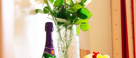 Una mesa con una botella de champán, una copa, un florero con flores blancas y una cesta de fruta.