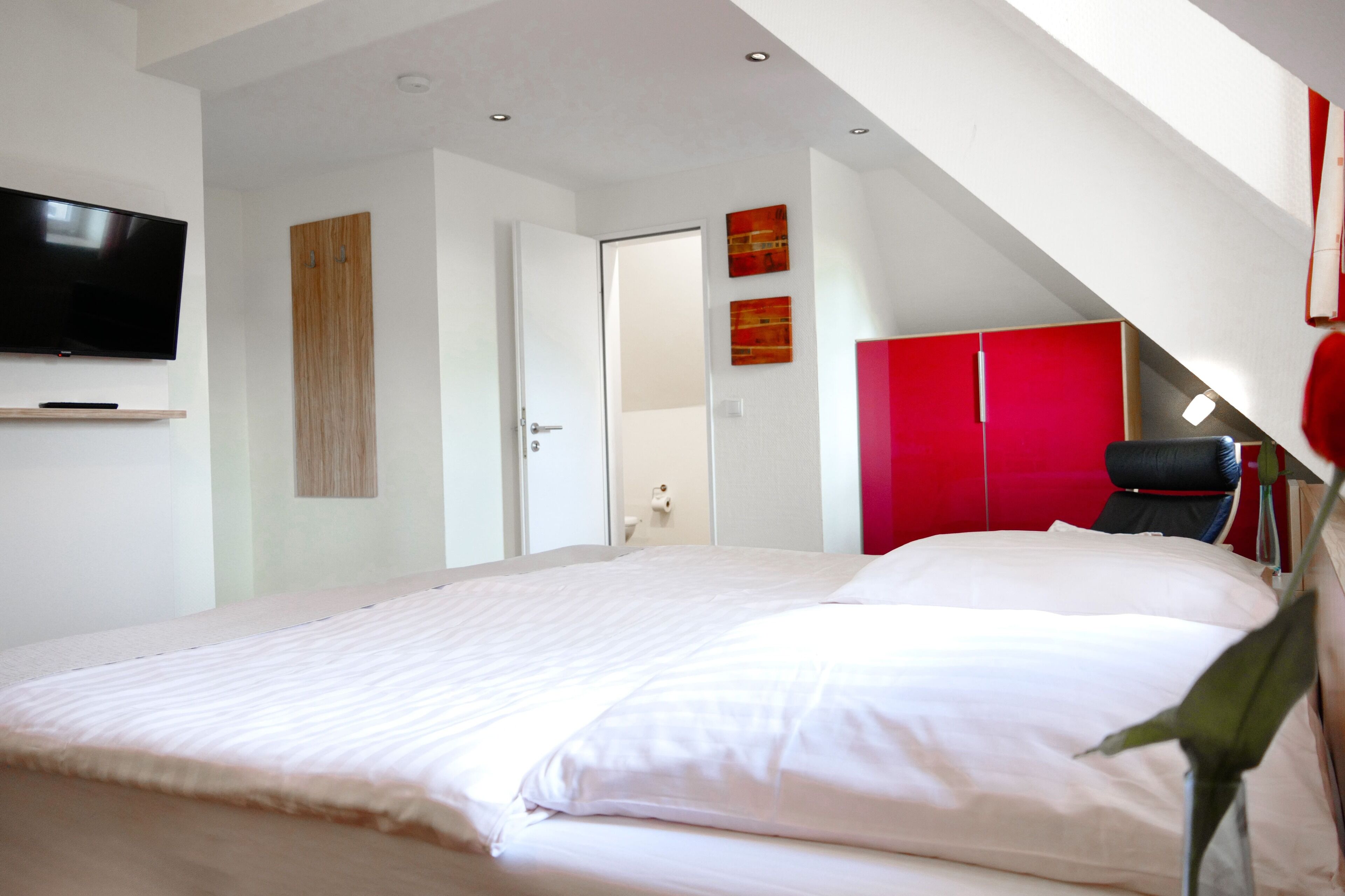 Un dormitorio con una cama grande, un televisor montado en la pared y un armario rojo.