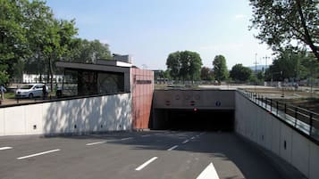 En tunnelindgang med piletavler på vejen, en hvid bil parkeret i nærheden og træer i baggrunden.