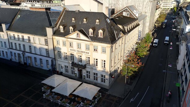 Un hotel con varios pisos, una entrada destacada y mesas exteriores con sombrillas.