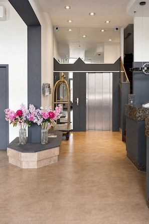 Un vestíbulo moderno con recepción, arreglo floral, ascensor y escalera.