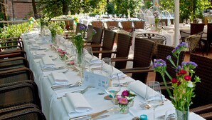 Un área de comedor al aire libre con sillas y mesas de mimbre preparadas para una comida.