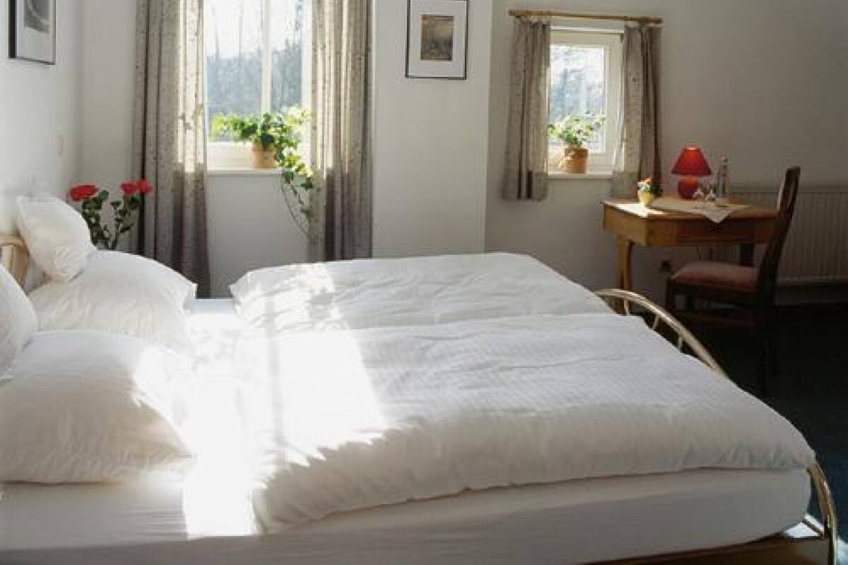 A bedroom with a bed, a desk with a chair, and a window with curtains.