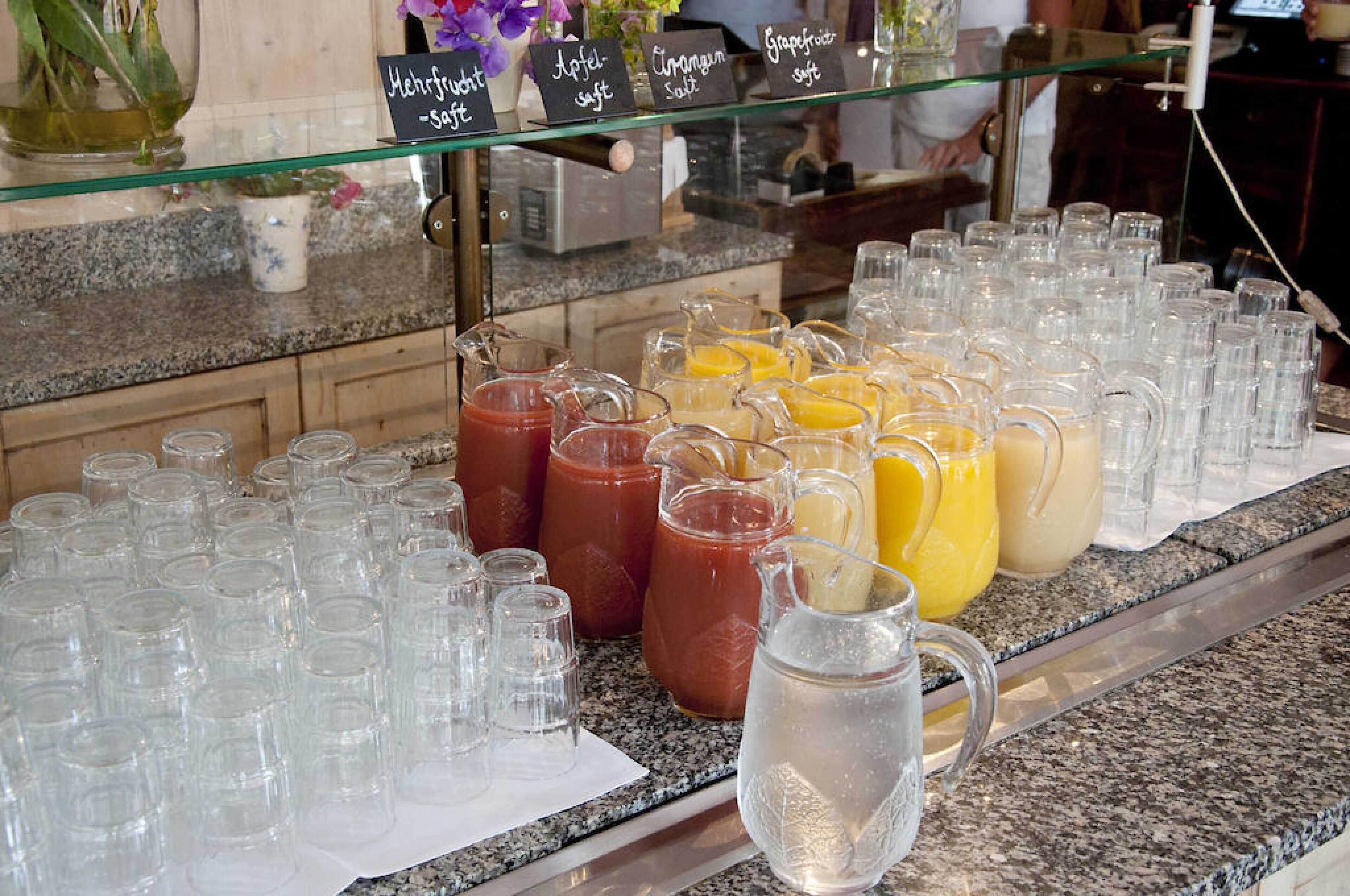 A beverage station with various drinks and empty glasses.