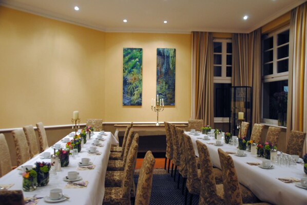 A dining room with long tables set for a meal, chairs, and two paintings on the wall.