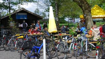 A park with bicycles parked and people sitting at tables under yellow umbrellas.