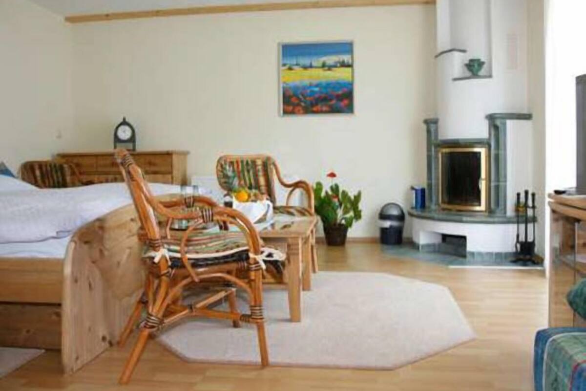 A cozy room with a bed, a wooden chair, a table with a plant, and a fireplace.