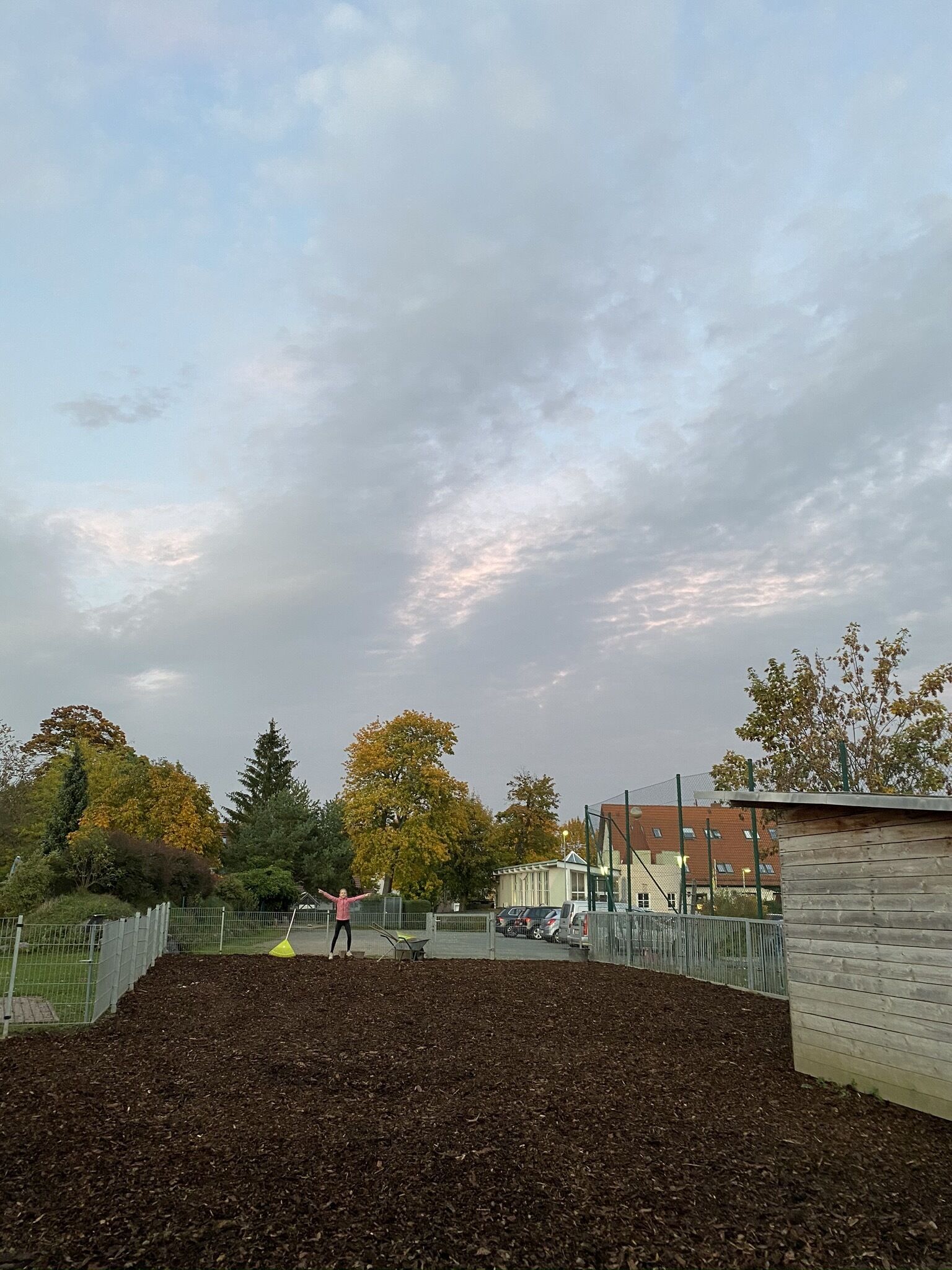 Un espacio al aire libre con un cerramiento, árboles y un edificio de fondo.