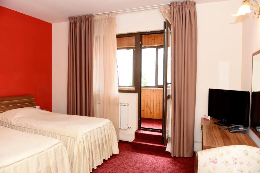 Habitación de hotel con dos camas, un televisor y vista a una terraza de madera a través de una puerta.