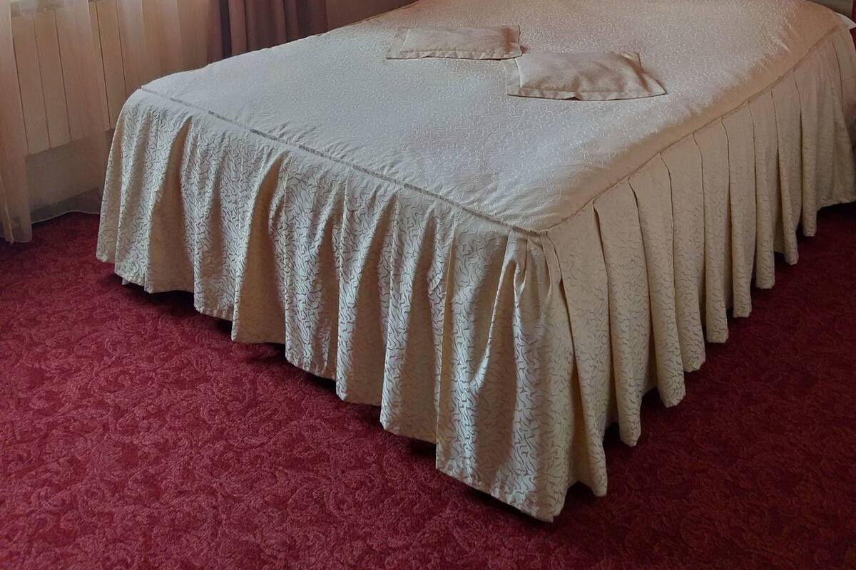 A bedroom with a bed, a window with curtains, a red wall, and a painting.