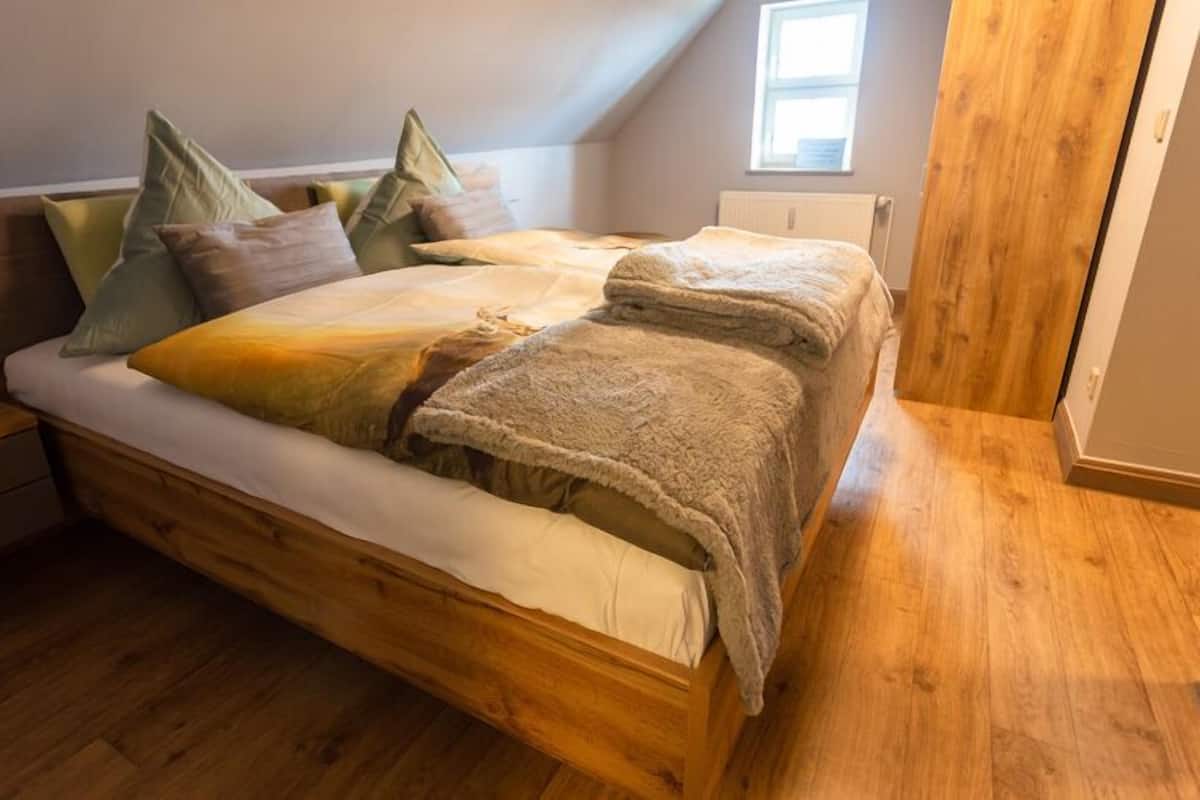Una cama de madera en una habitación con techo inclinado y ventana.