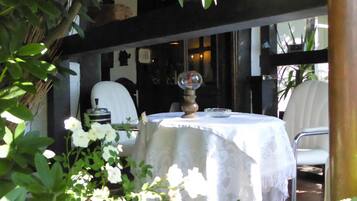 An outdoor dining area with a round table covered by a white tablecloth, surrounded by greenery and white flowers.