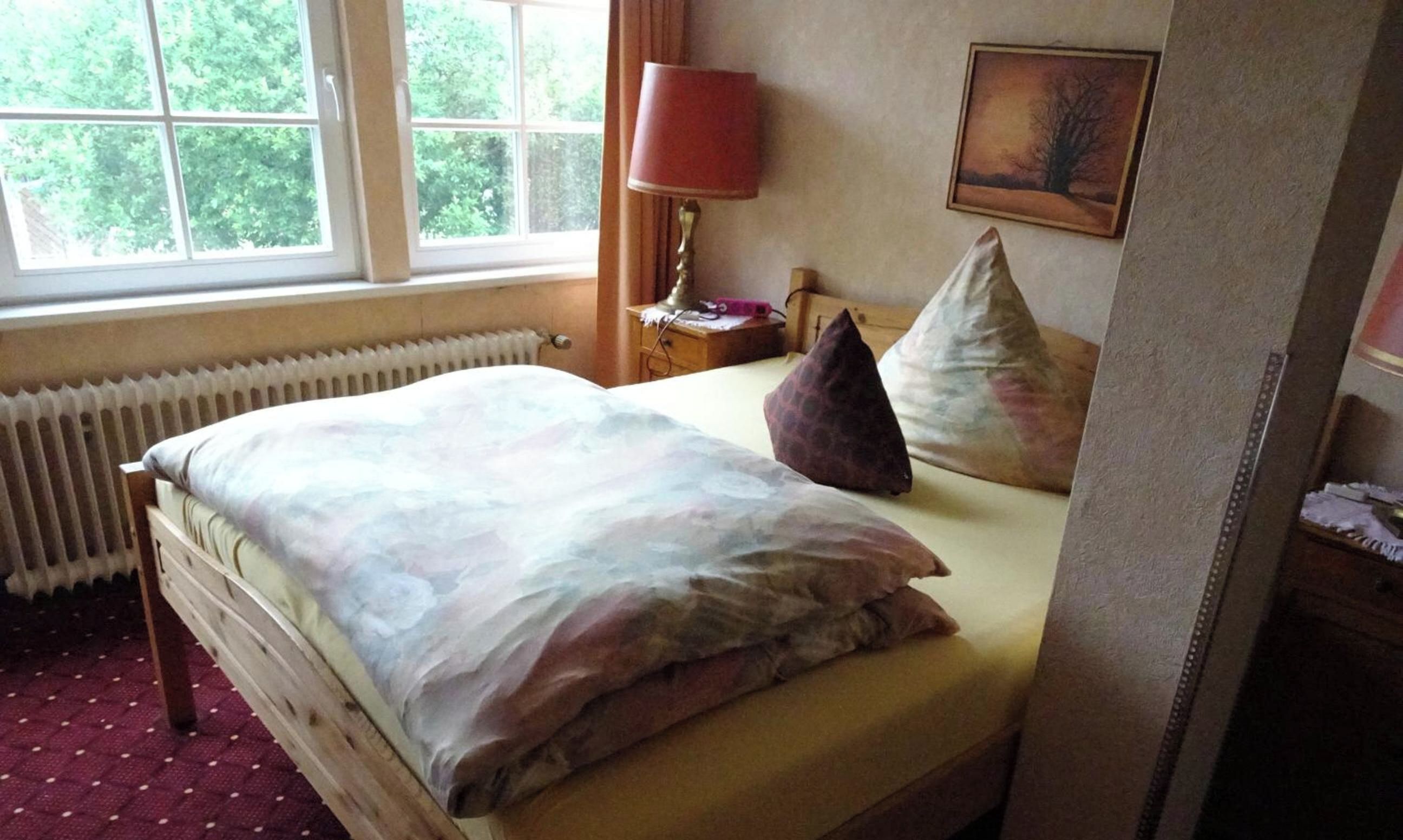 A bedroom with a bed, a window, a radiator, a lamp, and a painting on the wall.