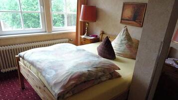 A bedroom with a bed, a window, a radiator, a lamp, and a painting on the wall.