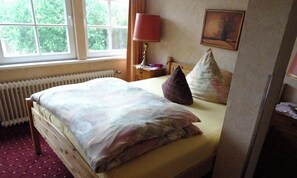 A bedroom with a bed, a window, a radiator, a lamp, and a painting on the wall.