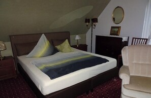 A hotel room with a bed, a chair, a lamp, a mirror, and a fireplace.