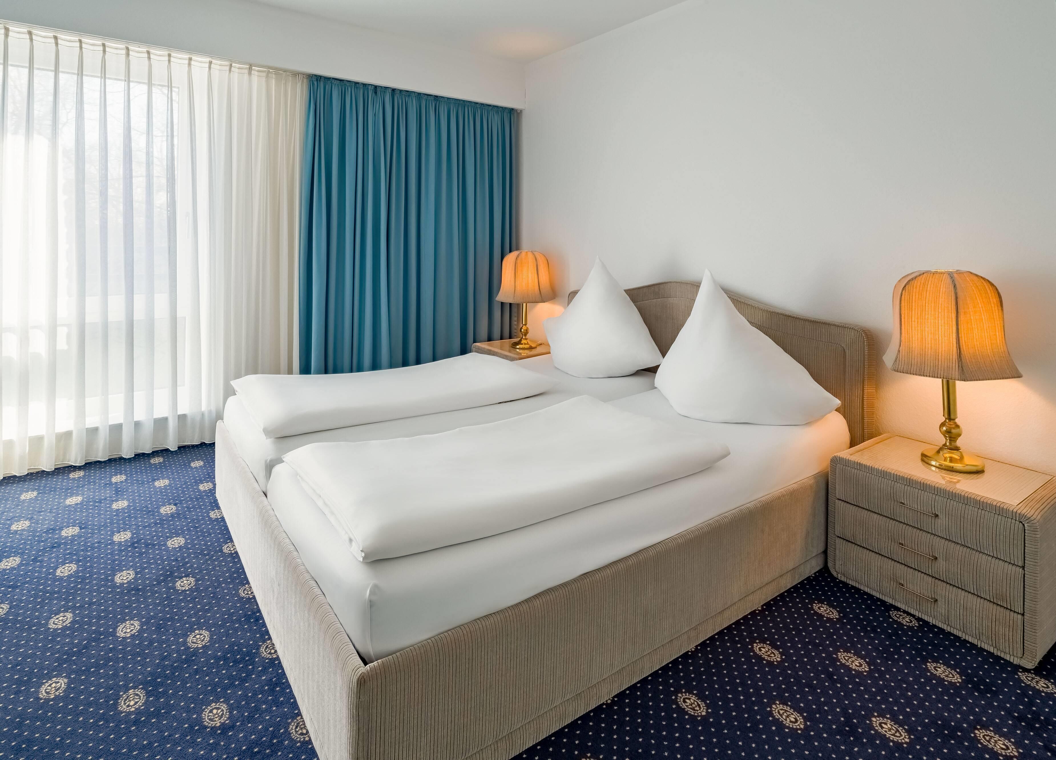 Una habitación de hotel con una cama grande, dos mesitas de noche y una mesita auxiliar con lámparas.