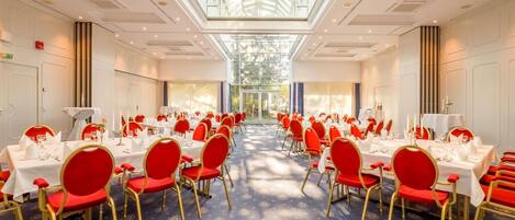 A large banquet hall with rows of tables and chairs, a high ceiling with a skylight, and a patterned carpet.