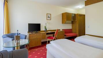 A hotel room with a bed, a desk with a chair, a television, a wardrobe, and a small table with a glass.