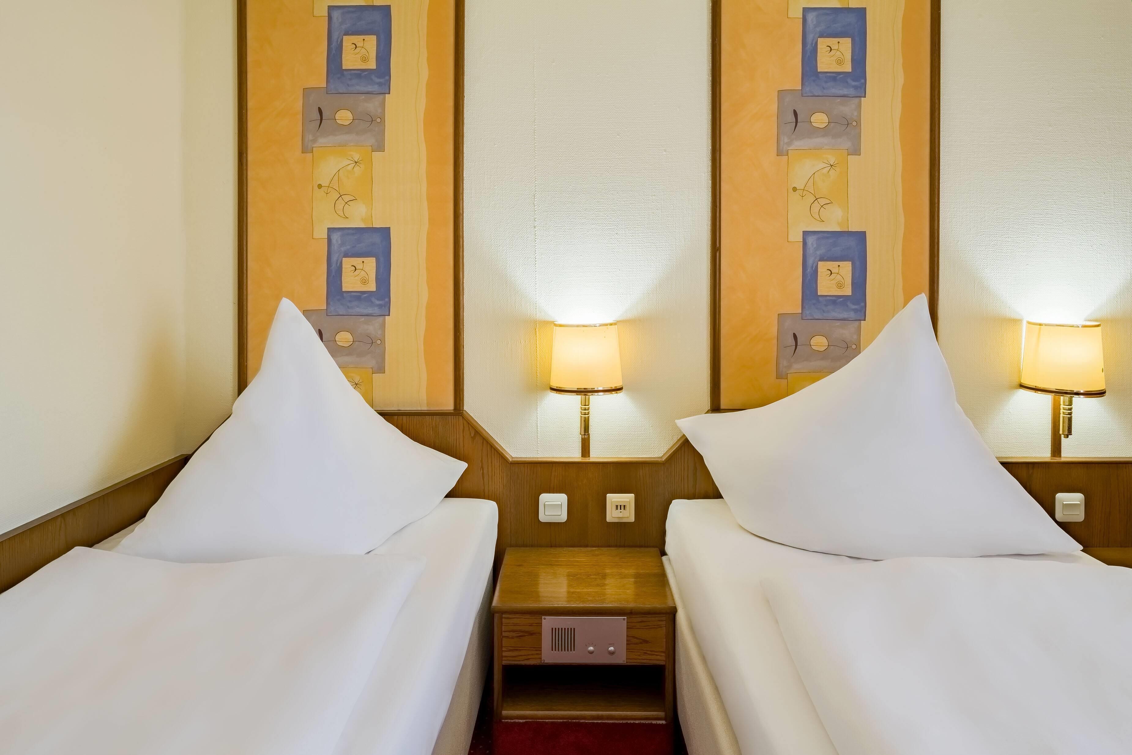 Habitación de hotel con dos camas individuales, cada una con una almohada y una mesita de noche.