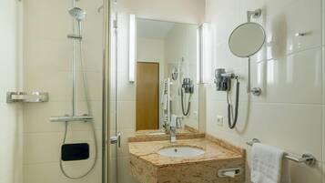 Un baño moderno con ducha envuelta en vidrio, lavamanos de mármol, cabezal de ducha de mano, secador de pelo portátil y un perchero para toallas.
