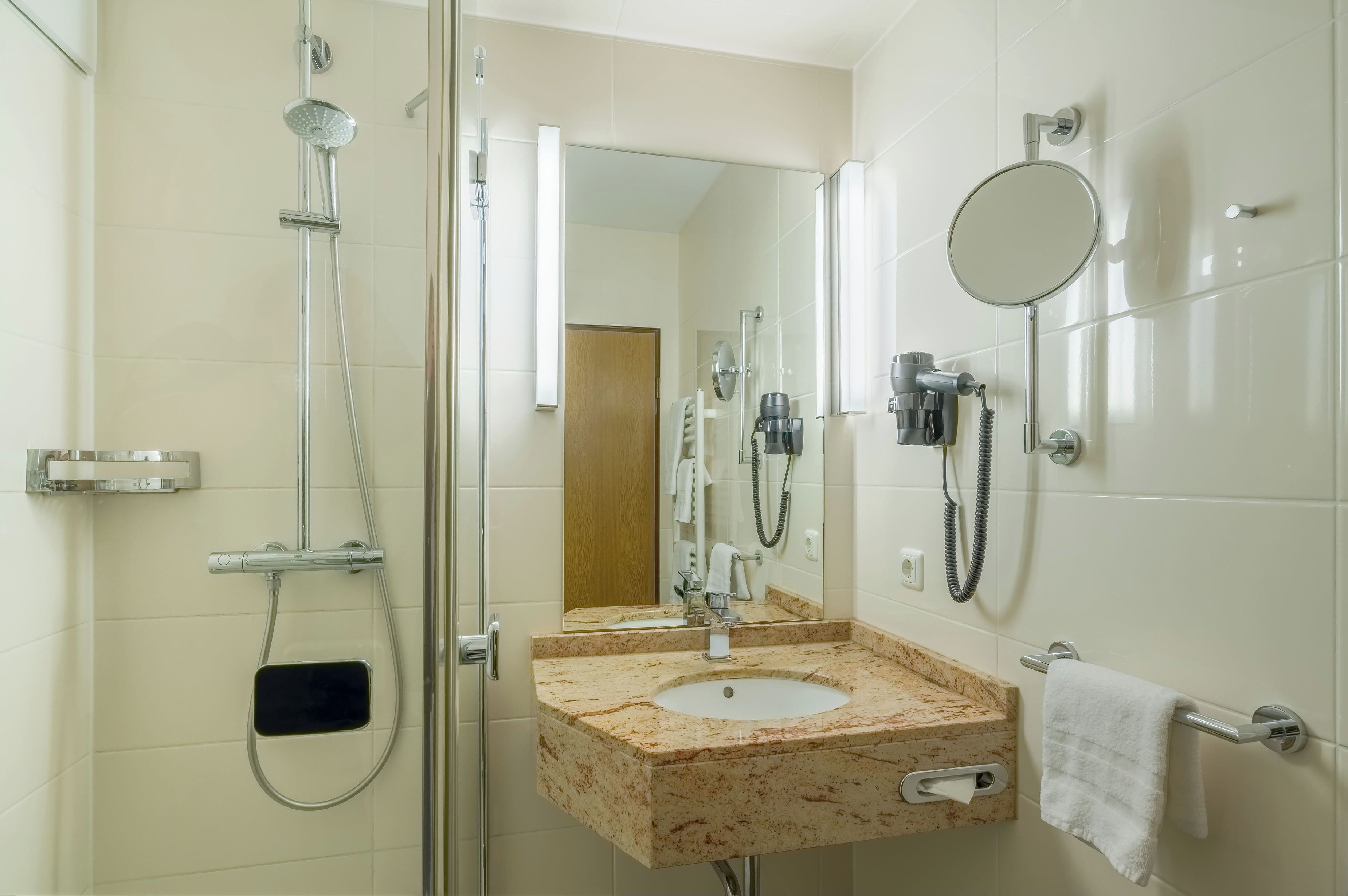 A modern bathroom with a glass shower enclosure, a marble sink, a handheld showerhead, a handheld hairdryer, and a towel rack.