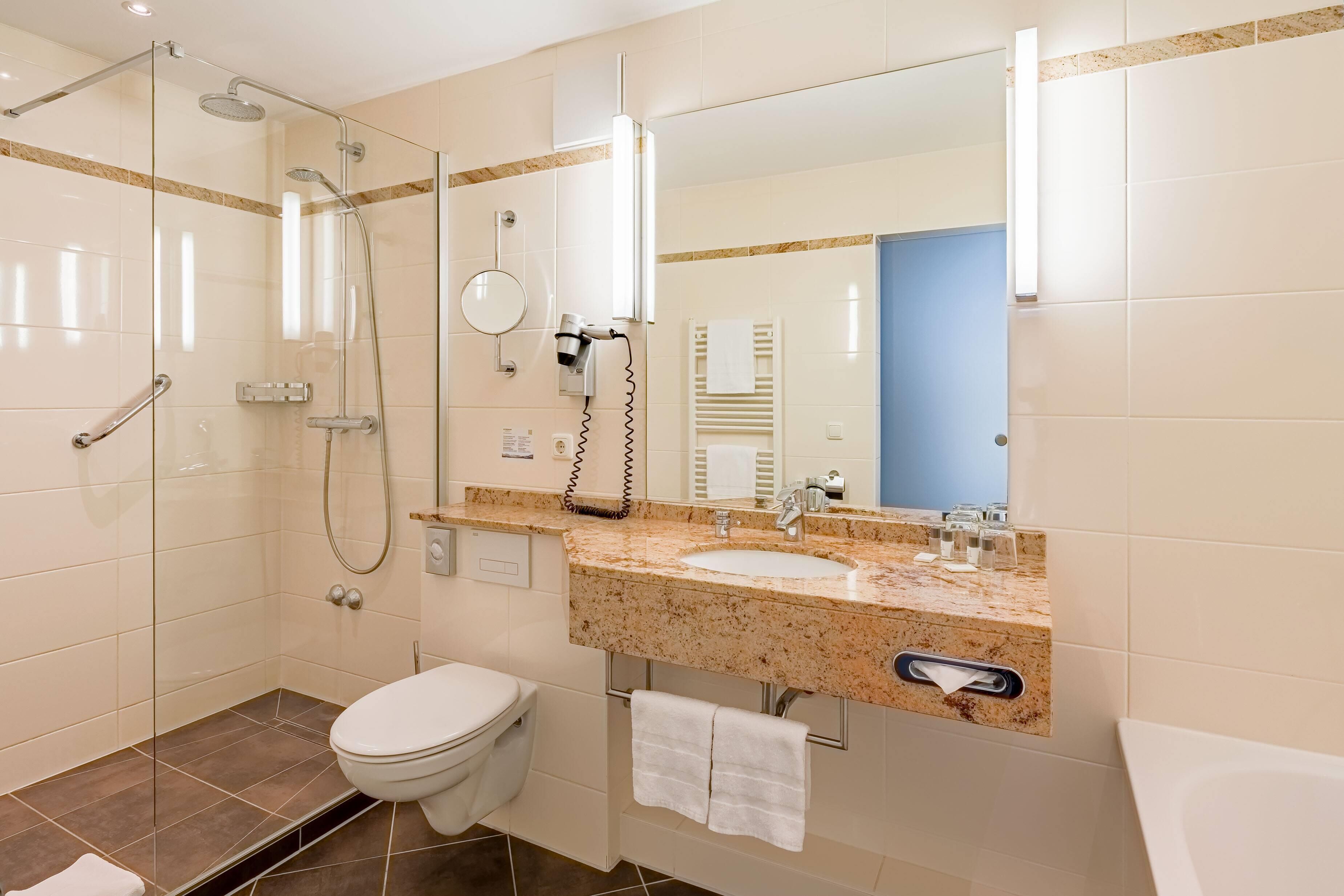 Un baño moderno con ducha envuelta en vidrio, inodoro e lavabo con encimera de mármol.