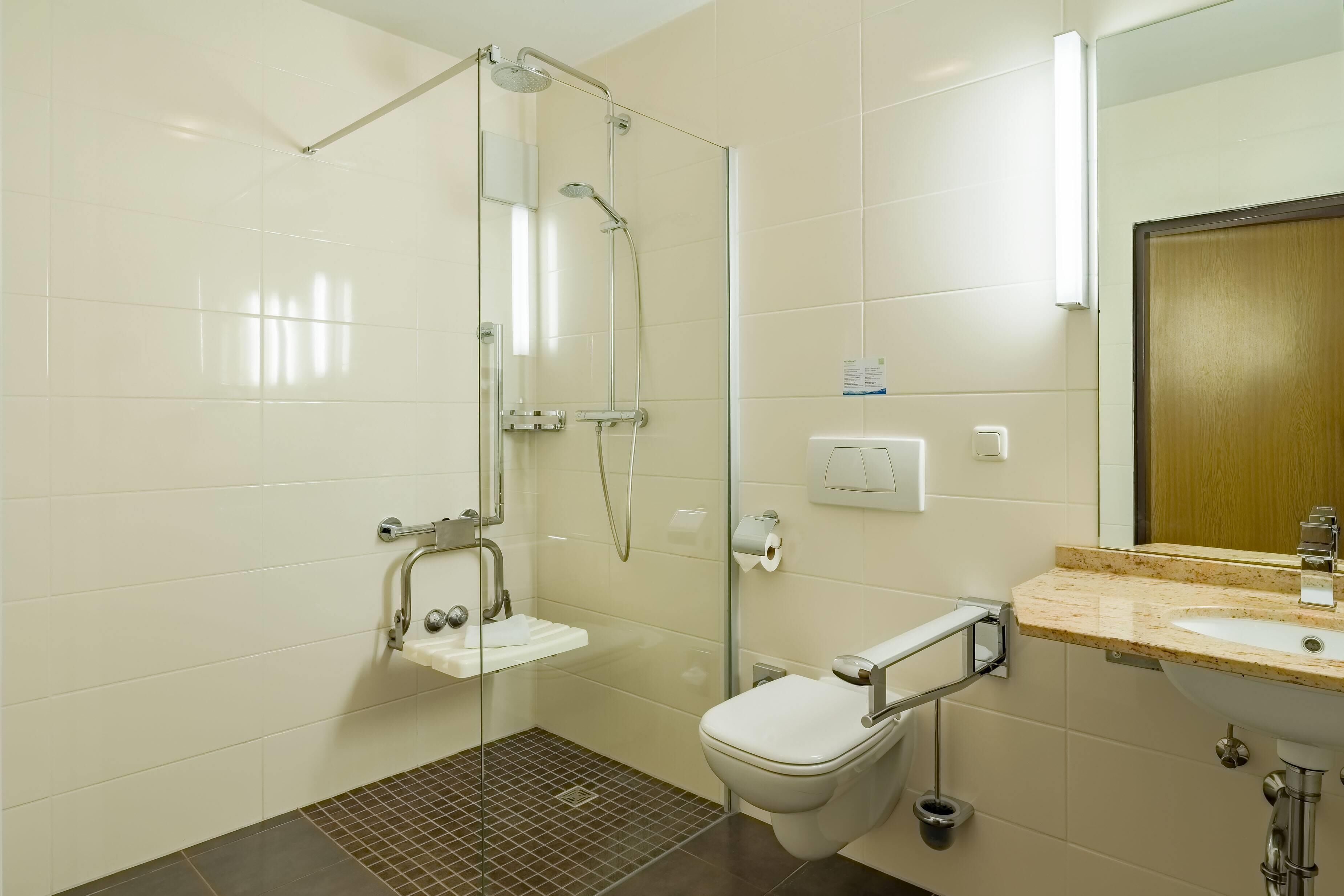 Un baño moderno con cabina de ducha de vidrio, un lavabo blanco con encimera de mármol y un inodoro con barra de apoyo.