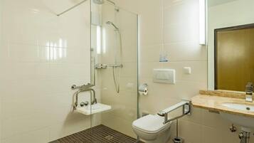 Un baño moderno con cabina de ducha de vidrio, un lavabo blanco con encimera de mármol y un inodoro con barra de apoyo.