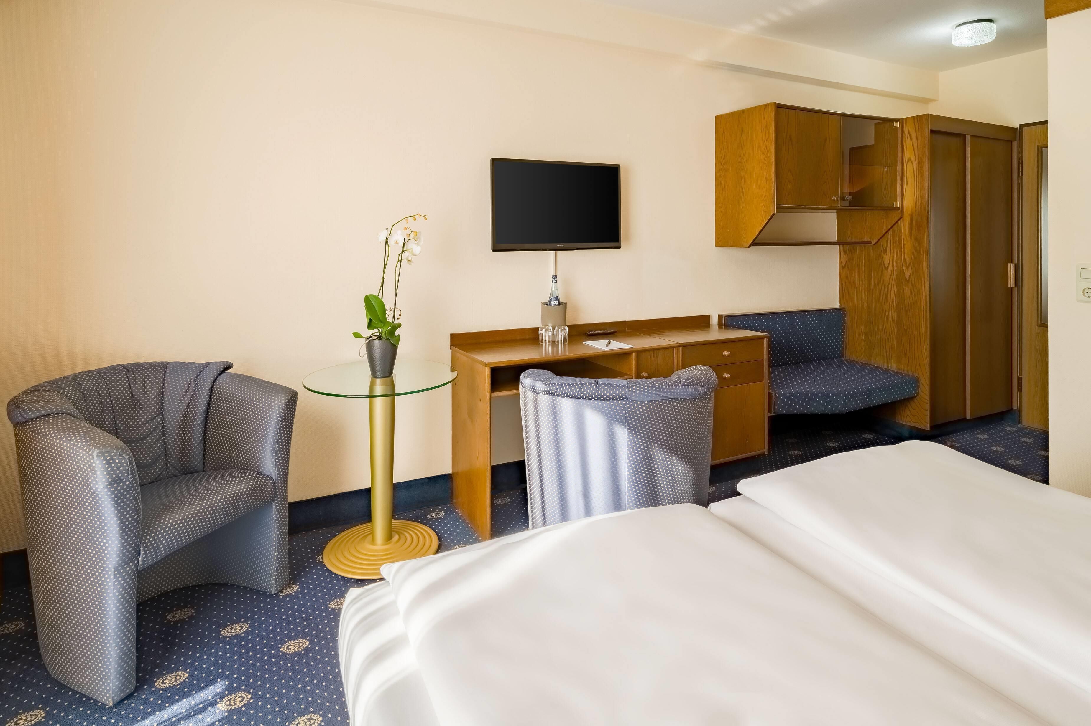 Ein Hotelzimmer mit einem Bett, zwei Sesseln, einem Schreibtisch mit Fernseher und einem Kleiderschrank.