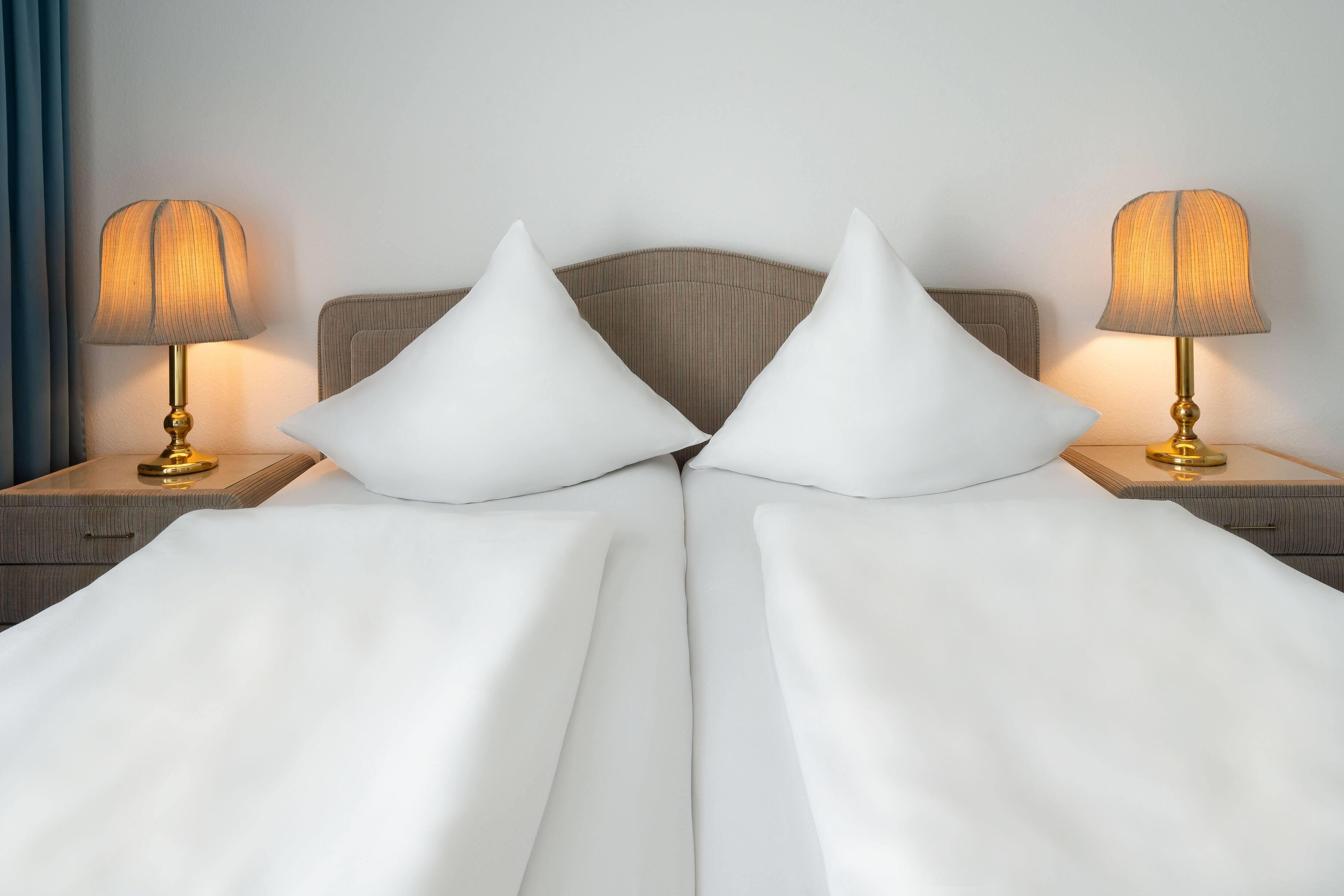 A neatly made bed with white linens and two pillows, flanked by two bedside tables with lamps.
