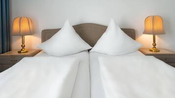 A neatly made bed with white linens and two pillows, flanked by two bedside tables with lamps.