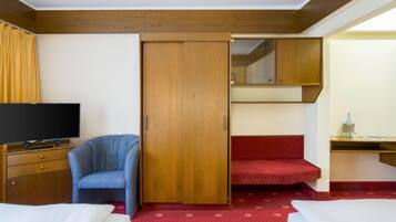 A hotel room with a TV, a blue chair, a wardrobe, a desk with a mirror, and a bed.