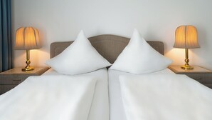 A neatly made bed with white linens and two white pillows, flanked by two bedside tables with lamps. - Aspire Oldenburg, Trademark Collection by Wyndham (Oldenburg)