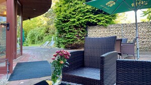 An outdoor seating area with wicker furniture, a green umbrella, and a vase with flowers. - Aspire Oldenburg, Trademark Collection by Wyndham (Oldenburg)