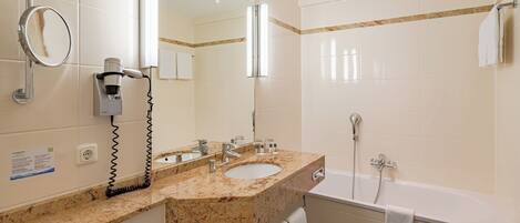 A modern bathroom with a granite countertop, a large mirror, a hairdryer, and a bathtub.