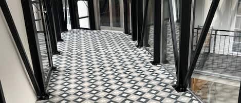 A corridor with patterned flooring and glass doors leading to a balcony.