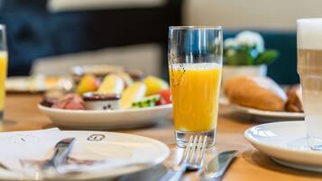 A breakfast setting with a glass of orange juice, a plate of food, and a cup of coffee on a wooden table.