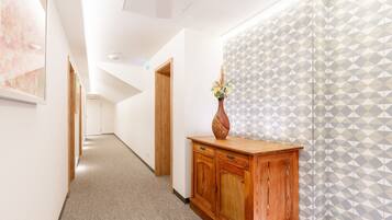 A hallway with a wooden cabinet, a vase with flowers, and a geometric patterned wall.