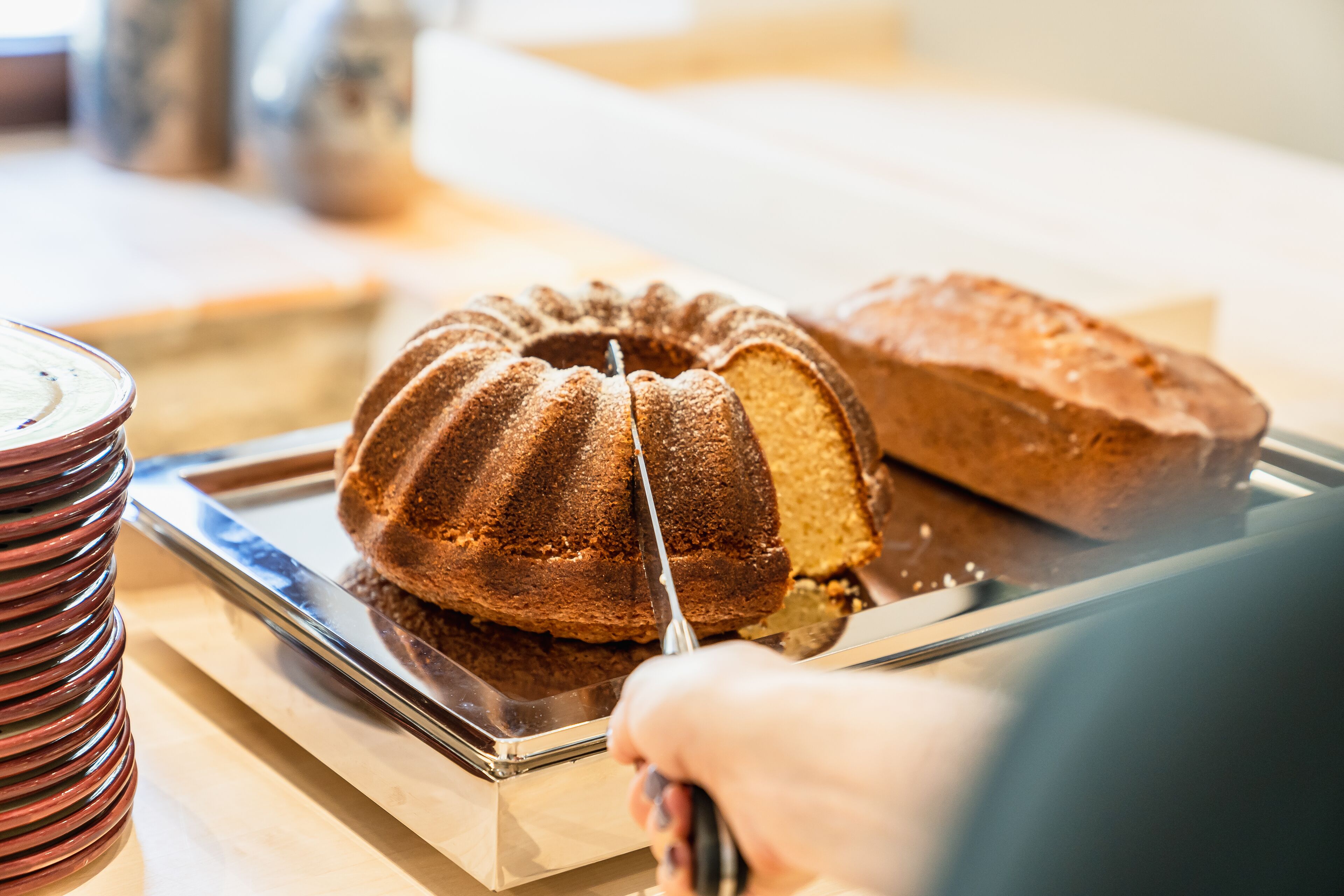 Un pastel bundt en una bandeja con un cuchillo cortándolo.