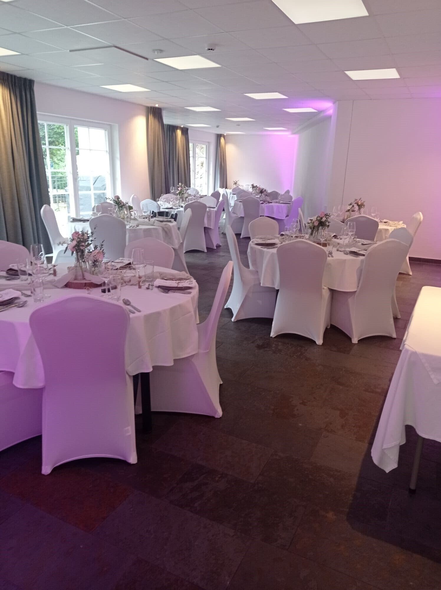 Une salle de banquet avec des tables rondes, des chaises blanches et un éclairage violet.