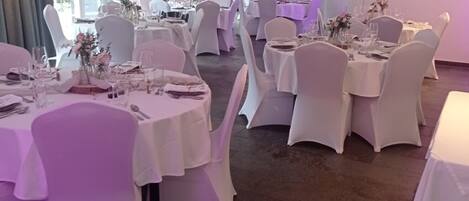 Une salle de banquet avec des tables rondes, des chaises blanches et un éclairage violet.