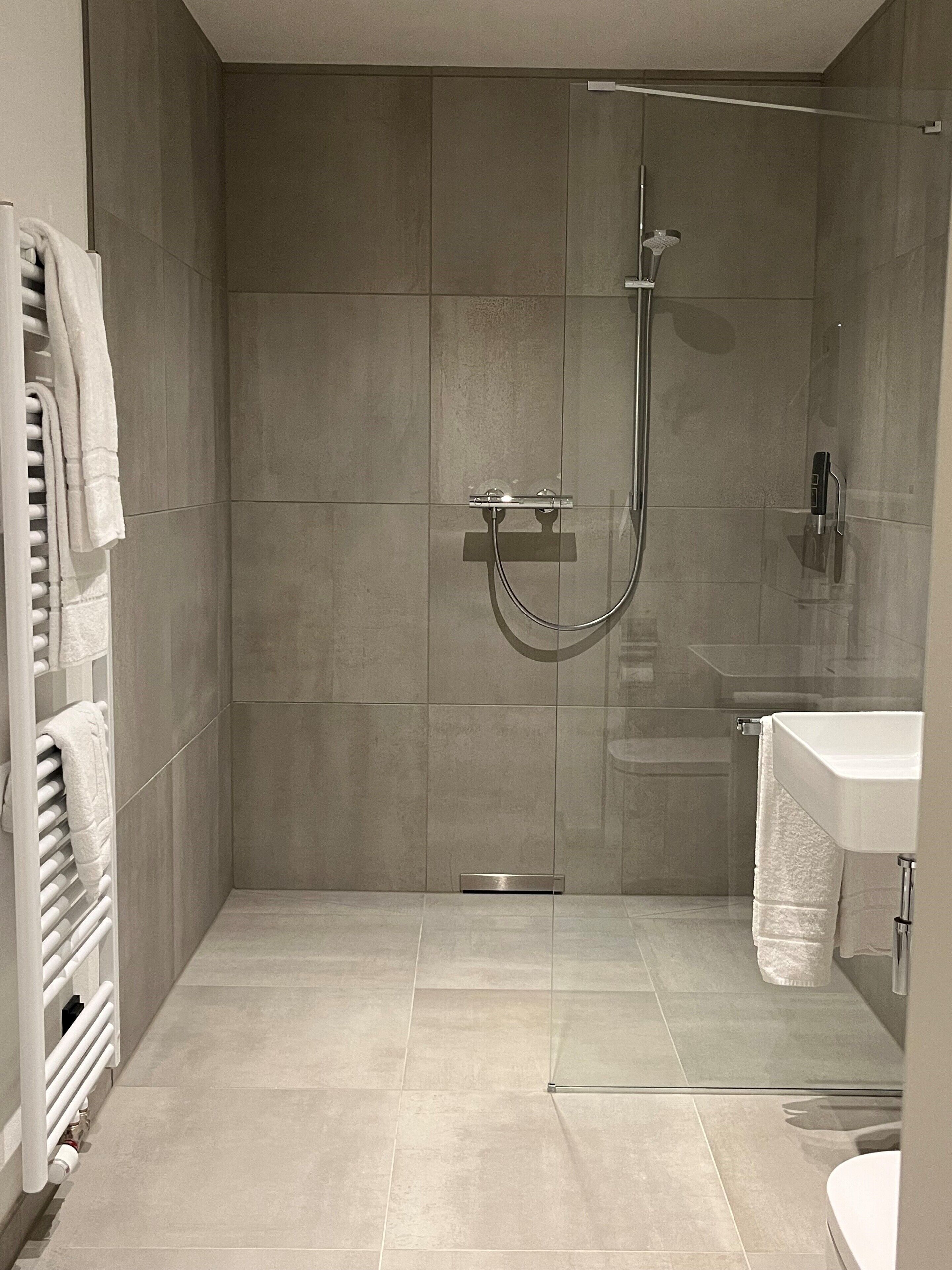 Un baño moderno con ducha envuelta en cristal, lavamanos blanco y toallero.