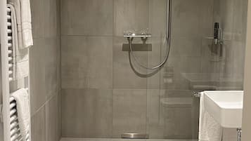 Un baño moderno con ducha envuelta en cristal, lavamanos blanco y toallero.