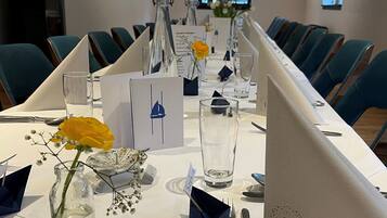 A conference room with a long table, chairs, and various items like a vase with a flower, a glass, and name cards.